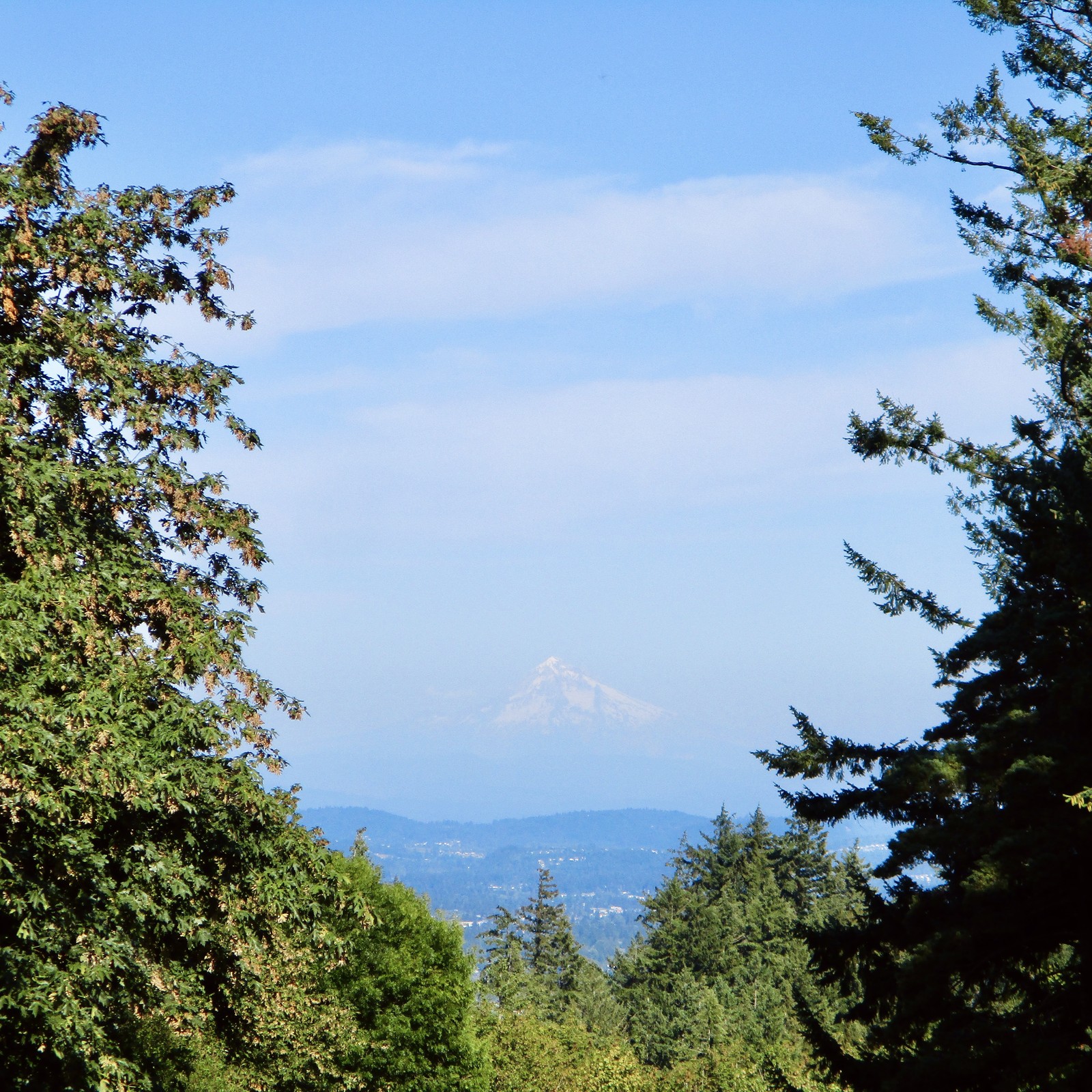 Conical volcanic peak obscured slightly by wildfire haze, on an otherwise sunny summer late afternoon