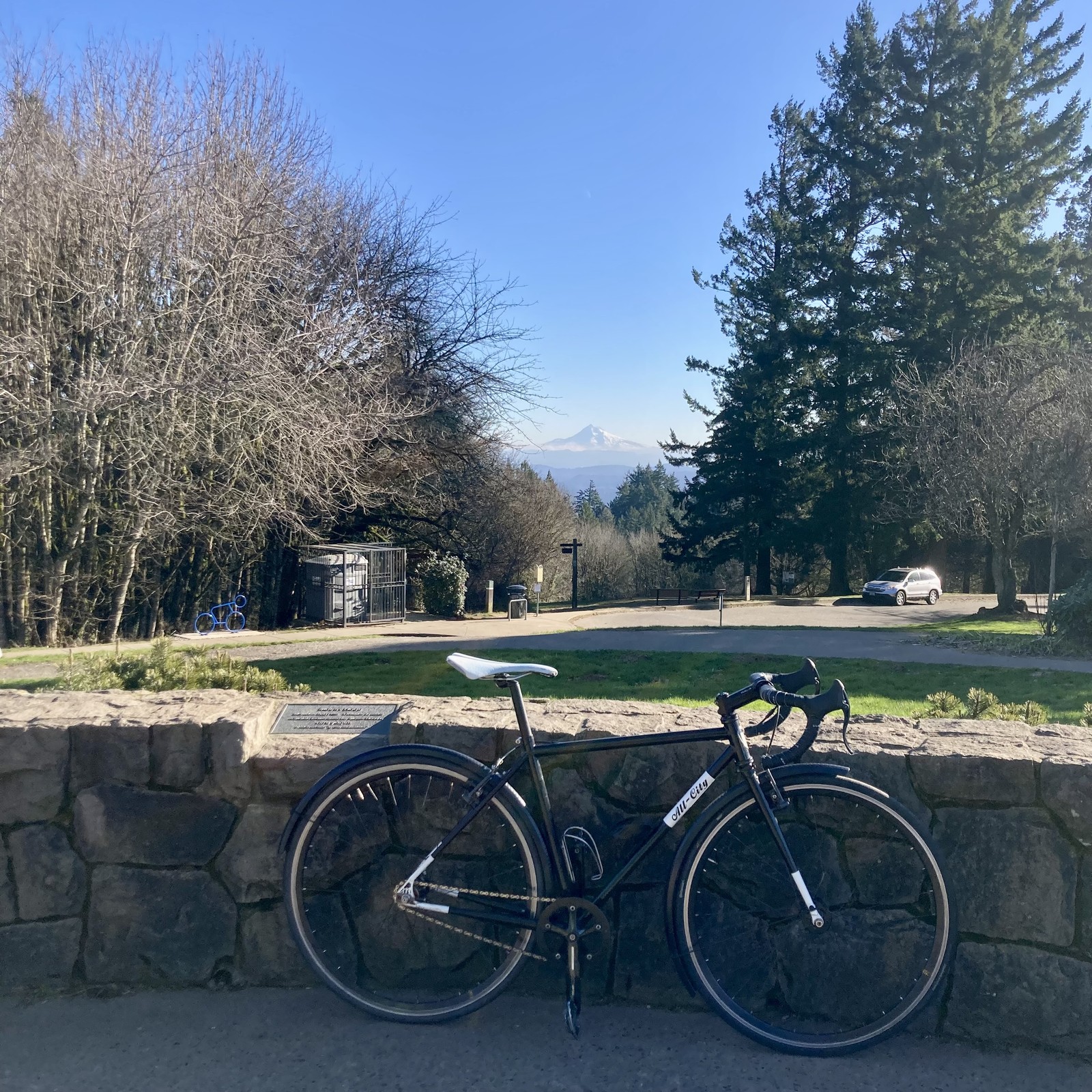 Single speed bike leaning against a low decorative stone wall with a snowy mountain in the distance, on a bright and windy day