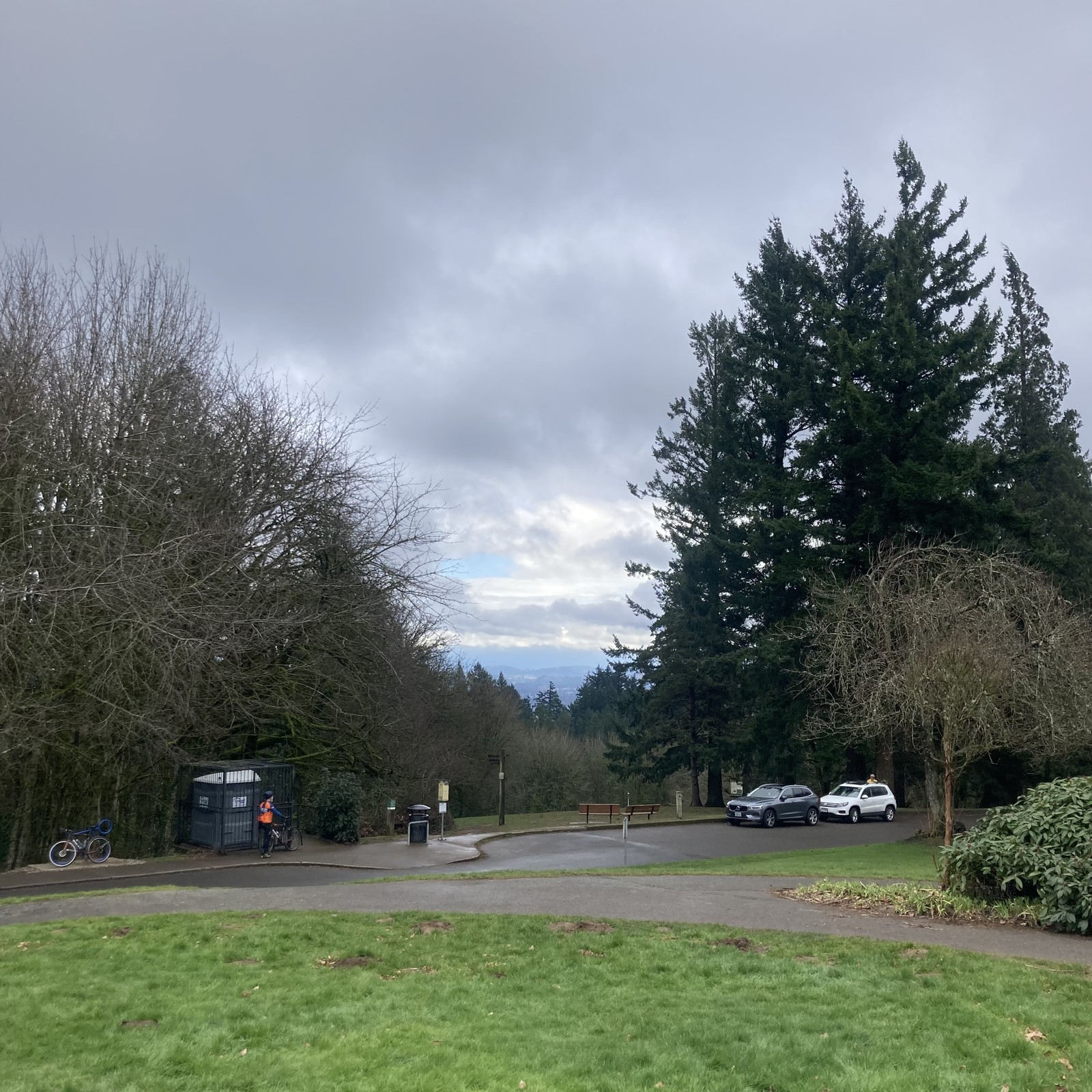 Wet gray sky. About 50' away a cyclist in Sellwood Cycles kit stands near a portypotty