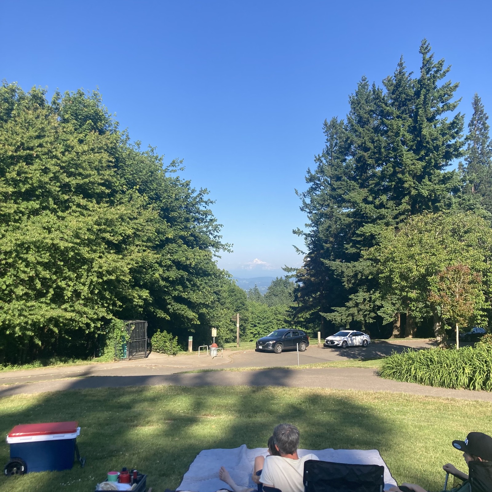 Mt. Hood, capped with snow & ringed with clouds, taken from Council Crest Park near sunset. In the foreground a German family has pitched a picnic, oblivious to (or uncaring of) having done so in one of the most-photographed places in Portland