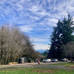 A cyclist in a bright pink jacket regards a lone snowy mountain in the distance under a blue sky streaked with high altitude clouds