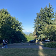 Mt. Hood on the eastern horizon as seen from Council Crest park at sunset. The mountain glows under a deep blue clear sky. Two people walk along a path in the foreground.