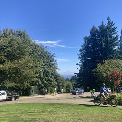 Mt. Hood as seen from Council Crest Park on a very clear late summer/early autumn afternoon. In the foreground a dad and preschool-age kid ride past on an electric cargo bike