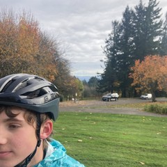 View toward Mt. Hood from Council Crest, the base of the mountain is visible under a deck of stratus clouds. The background is out of focus; in the foreground & corner of the frame is a young man in a bike helmet looking out of frame