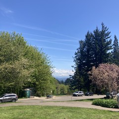 Mt. Hood, capped with a growing thunderhead, under a brilliant sky crisscrossed with contrails. Taken from Council Crest Park. A cargo bike is parked about 100' downhill. Vegetation is brilliant green